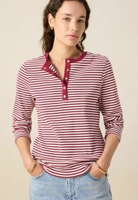 Rot-weiß gestreiftes langärmliges T-Shirt mit Henley-Ausschnitt und Knopfleiste mit drei Knöpfen; aus geripptem Stoff gefertigt.