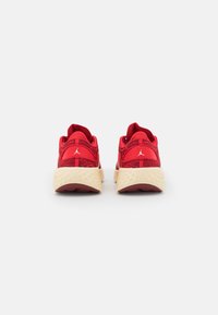 Une paire de chaussures de sport rouges avec des semelles beiges texturées, vue de l'arrière, avec un petit logo blanc sur chaque talon.