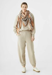 Ensemble de vêtements d'intérieur beige composé d'un sweat-shirt à col rond et d'un pantalon à taille élastique, associé à une écharpe à motifs ornée d'accents imprimés animaliers.