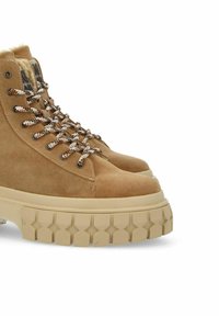 Stivaletti alla caviglia in suede beige con suola spessa beige, dotati di occhielli metallici per i lacci, lacci a motivi marroni e bianchi, e fodera in morbido pelo.