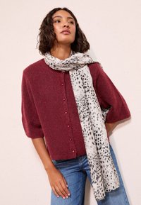 Bordó rövid ujjú kardigán kerek nyakkivágással és rózsaszín gombokkal, szürke sállal párosítva, amelyen fekete leopárdminták találhatók.