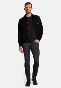 Veste en daim noir avec fermeture à boutons, associée à un t-shirt noir, un jean slim foncé et des baskets noires brillantes. Look simple et décontracté.
