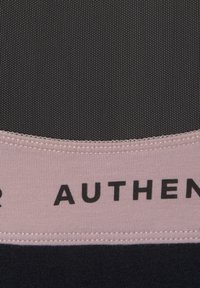 Schwarzer und pinker Sport-BH aus strukturiertem Stoff. Mit einem breiten pinken Band, auf dem in fetten schwarzen Buchstaben das Wort "AUTHENTIC" steht.
