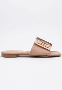 Sandalia plana de color nude con una correa de cuero suave que presenta una hebilla cuadrada metálica dorada. Suela plana, diseño minimalista, punta abierta.