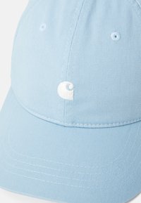 Casquette de baseball bleu clair avec une texture côtelée et un logo brodé blanc à l'avant, présentant une visière courbée et six œillets de ventilation.