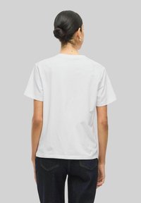 Vit bomullströja med korta ärmar. Standard design med rund hals. Slät textur. Buren med mörka jeans. Bakifrån.