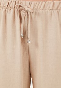 Beige elastische taillebroek met een trekkoord en decoratieve zilveren accenten. Zachte textuur, lichtgewicht stof en een ontspannen pasvorm.