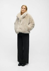 Faux fur beige jakke med bred krave, knaplukning og sidelommer, parret med højtaljede sorte vidde jeans og sorte sko.