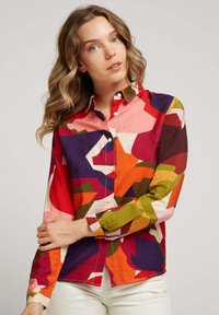 Chemise à boutons colorée avec un design en patchwork dans des teintes de rouge, rose, vert et violet, fabriquée à partir d'un tissu texturé.