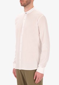 Camicia a maniche lunghe di colore rosa chiaro con colletto a bande, dotata di una chiusura frontale con bottoni e polsini, realizzata in un tessuto morbido e liscio.