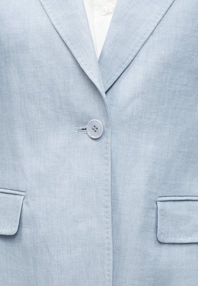 Φωτεινό γαλάζιο σακάκι με ένα κουμπί πάνω από λευκό πουκάμισο, με σχισμές στο πέτο και δύο τσέπες με καπάκι στο μπροστινό μέρος.
