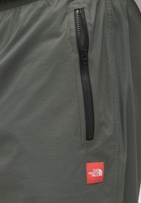 Βερμούδα σε ελαιόχρωμο με υφή, που διαθέτει μαύρη τσέπη με φερμουάρ και κόκκινο λογότυπο της The North Face στο  πλάι.