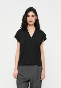 Haut noir à manches courtes avec un col en V, coupe décontractée, fabriqué en tissu léger, présentant un design épuré et minimaliste ainsi qu'une texture lisse.