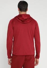 Sudadera roja de manga larga fabricada con un tejido ligero y texturizado. Cuenta con capucha y un diseño sin costuras con costuras planas.
