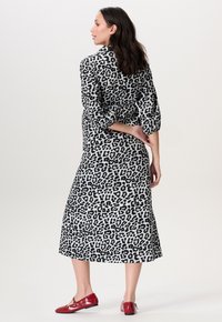 Luipaardprint jurk in zwart en wit, met driekwart mouwen en een middellange zoom, gecombineerd met rode flats.