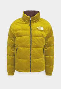 Gul vadderad bomberjacka i manchestertyg med hög krage, dragkedja framtill, två sidofickor och en vit logotyp på vänster bröst.