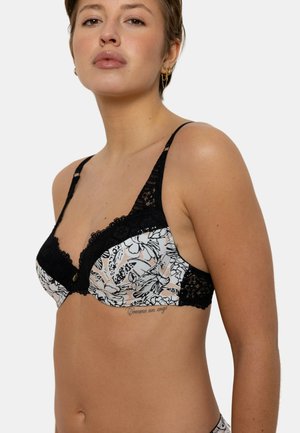 Soutien-gorge noir à motifs floraux, bordé de dentelle, avec des bretelles réglables ; il présente un bouton décoratif au centre et un design semi-transparent.
