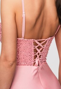 Vue de dos d'une femme portant une robe style corset rose à paillettes avec un laçage dans le dos et de fines bretelles ajustables.