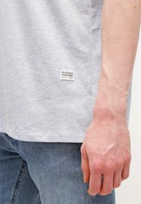 Světl gray bavlněné tričko s krátkým rukávem, na dolní straně s etiketou G-Star. V páru s modrými denimovými džíny.