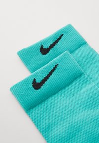 Türkise Nike-Socken mit strukturiertem Strickmuster, versehen mit einem schwarzen bestickten Logo am Bündchen. Jede Socke hat ein breites, weiches Band.