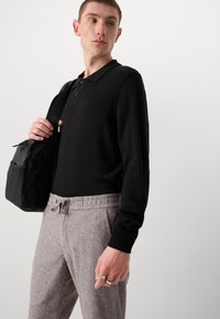 Črna polo majica s tremi gumbi in rebrastimi manšetami, v kombinaciji z svetlo sivo različico hlač, ki imajo elastičen pas in vrvico.