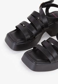 Sandali platform neri con molteplici cinturini piatti e larghi e design con punta quadrata. Realizzati in pelle liscia con una soletta testurizzata e tacco largo.