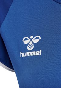Blå atletisk T-shirt med tekstureret stof, der har et hvidt emblem og "hummel" logo nær halsudskæringen. Korte ærmer, rund hals design.