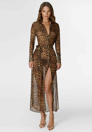 Femme portant une robe longue transparente à manches longues imprimée léopard avec une fente haute et une ceinture nouée à la taille, associée à des sandales dorées à talons hauts.