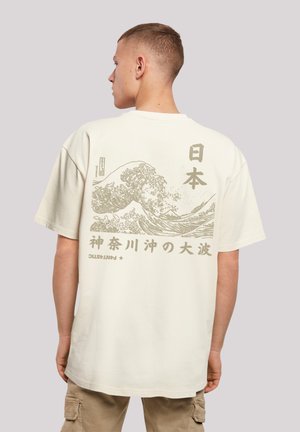 Camiseta de algodón beige con un gran gráfico de una ola y texto japonés impreso en marrón claro en la parte posterior. Mangas cortas y corte relajado.