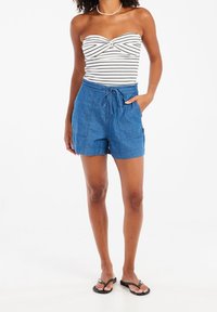 Denim shorts with a relaxed fit, featuring a drawstring waist, side pockets, and a light blue hue, paired with a striped tube top.