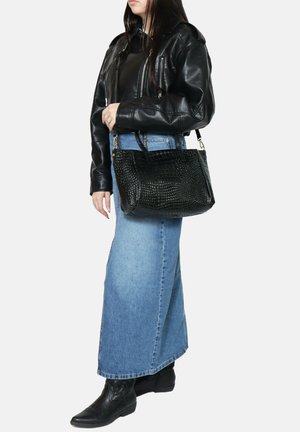 Zwarte leren handtas met een gestructureerde afwerking met krokodillenpatroon. Beschikt over korte handvatten en een licht afgeronde vorm. Draagt bij een denimrok.