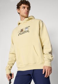 Yellow hoodie made from soft fabric featuring a front pocket. It has playful graphics and text on the chest, with long sleeves and a hood.