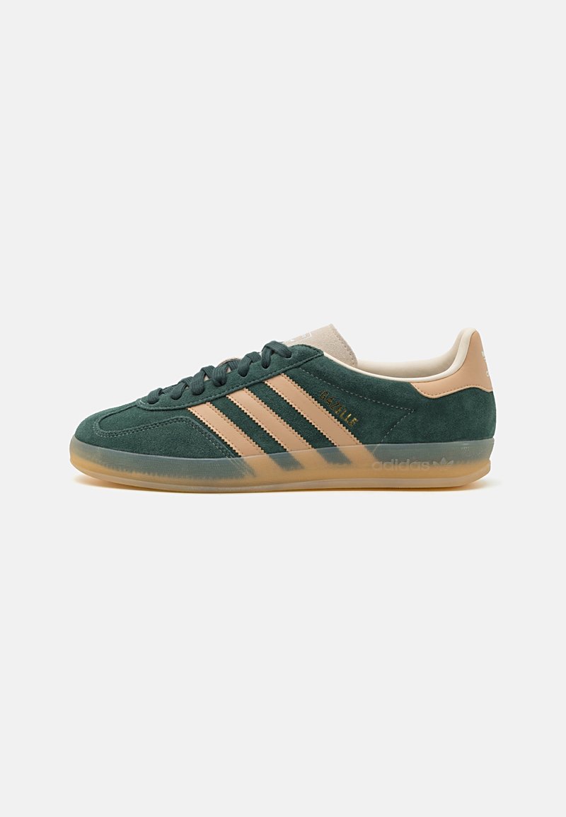 Green suede sneakers with beige accents, featuring three stripes and a translucent gum sole. Gold "Gazelle" branding on the side.