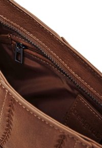 L'interno della borsa in pelle marrone presenta una chiusura con zip con cuciture a rilievo. La fodera è in un tessuto marrone scuro uniforme. I dettagli includono un'etichetta del marchio.