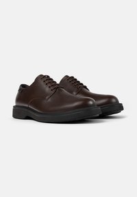 Pantofi din piele maro, cu șireturi, cu un finisaj neted, vârf rotund și o talpă din cauciuc negru, având șase găuri pentru șireturi și detalii minime de cusătură.