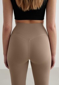 Augsti jostoti, bēši leggins ar gludu tekstūru un minimālu šuvju izpildījumu, kas izstrādāti komfortam un elastībai.