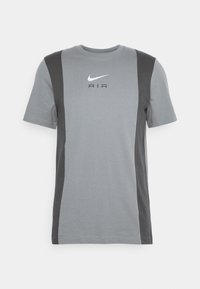 Šedé tričko s tmavě šedými bočními panely, kulatým výstřihem a bílým logem Nike. Tkanina má hladkou texturu, vhodnou pro volnočasové nošení.