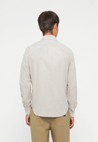 Stripet langermet skjorte i lys beige og krem, med standard krage, knapped cuffs og avrundet hem. Teksturlignende stoff.