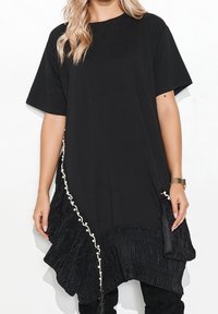 Czarna, oversize sukienka-t-shirtem z krótkimi rękawami, z falbaniastym dołem i perłowymi zdobieniami wzdłuż jednej strony.