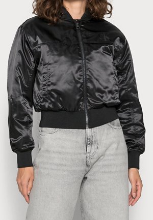 Schwarze Bomberjacke aus Satin mit durchgehendem Reißverschluss, gerippten Bündchen und Bund. Verfügt über ein dezentes Logo auf der linken Schulter.