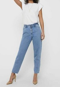 Blue denim high-waisted jeans with a gathered waistband, featuring front buttons and side pockets, paired with a white t-shirt.