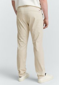 Jasno beżowe bawełniane spodnie o prostym kroju, z tylnymi kieszeniami i minimalistycznym wzornictwem. Noszone z białymi sneakersami.