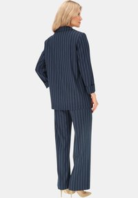 Granatowa marynarka w prążki i szerokie spodnie zestaw, z wykrojonym kołnierzykiem, długimi rękawami i miękkiego materiału. W połączeniu z jasnymi butami.