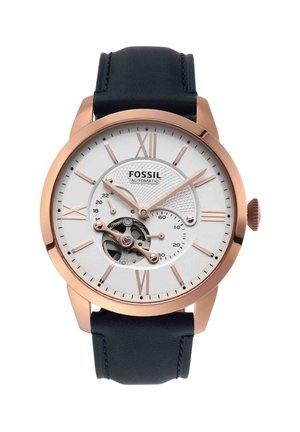 Montre automatique pour homme Fossil avec boîtier en or rose, cadran blanc, chiffres romains, engrenages visibles et bracelet en cuir noir.