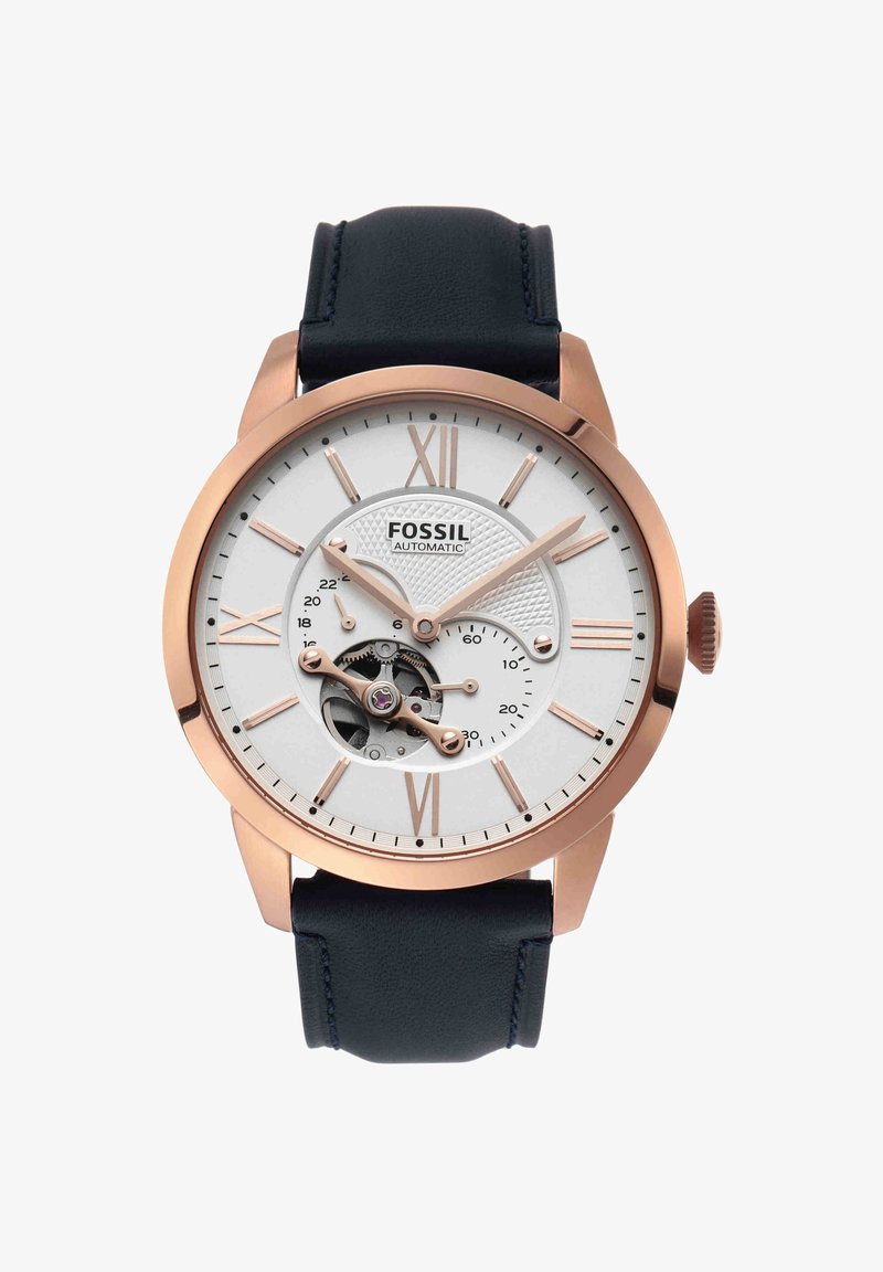 Montre automatique pour homme Fossil avec boîtier en or rose, cadran blanc, chiffres romains, engrenages visibles et bracelet en cuir noir.