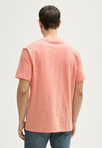 Lyserød koralfarvet kortærmet T-shirt lavet af tekstureret stof, med runde halsudskæring og en afslappet pasform, parret med blå jeans.