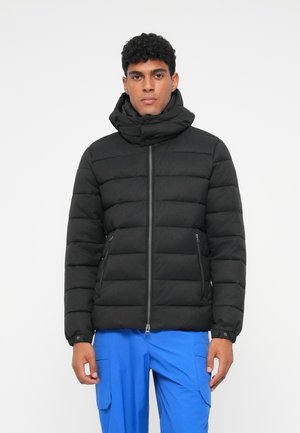 Svart puffjacka med hög krage, dragkedja fram och dragkedjefickor på sidorna. Texturerad, kviltad design med en lätt känsla.