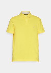 Keltainen polo-paita, jossa on lyhyet hihat, kaulus, kaksinappinen etumus ja pieni logo rinnassa. Valmistettu sileästä puuvillakankaasta.