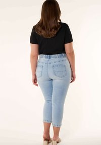 Jeans skinny bleu clair avec une taille élastique haute, deux poches arrière et une coupe courte, associés à un haut noir à manches courtes.