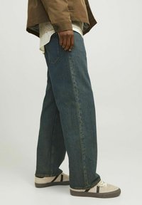 Laiad sinised denim püksid tekstureeritud viimistlusega ja klassikalise viie taskuga disainiga, koos beežide tossudega mustade aktsentidega.